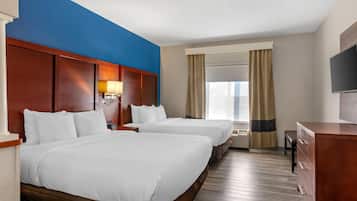 A hotel room with two beds, a wooden headboard, a TV, a desk, and a window with curtains.