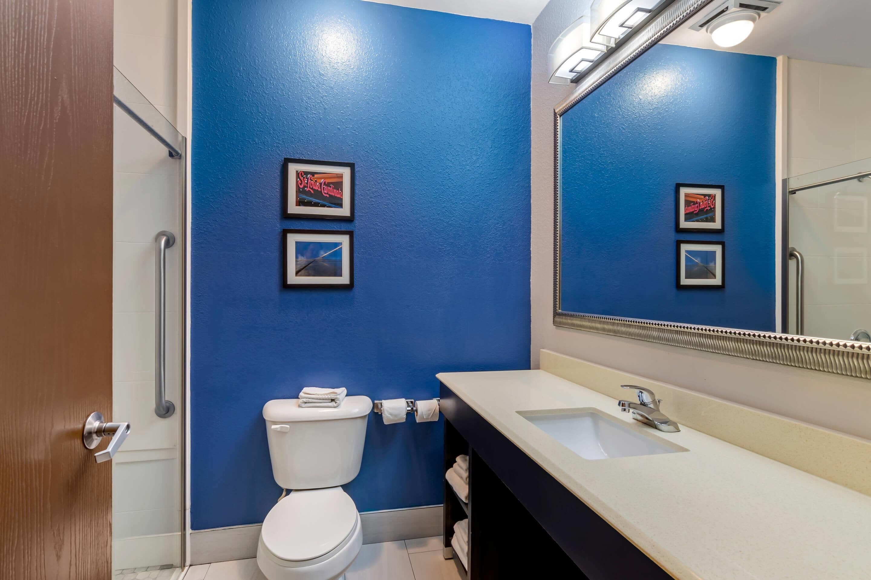 A bathroom with a blue wall, a white toilet, a sink, and a mirror.