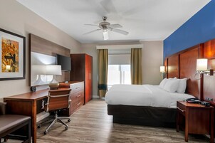 Habitación de hotel con cama, escritorio, silla, televisor y ventilador de techo.