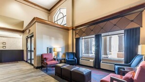 Un hall d’hôtel avec un plancher en bois, un comptoir de réception, deux fauteuils, un canapé et de grandes fenêtres donnant sur les bâtiments environnants.