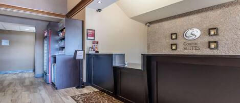 A hotel reception area with a dark reception desk, a clock, and a sign for 'Comfort Suites'.