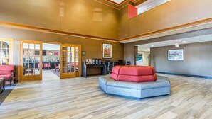 Un hall d’entrée avec un plancher en bois, un comptoir de réception, un espace détente avec un canapé rouge et une porte en verre donnant sur une autre pièce.