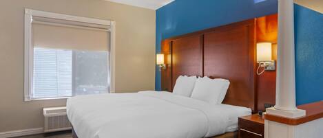 A hotel room with a large bed, a nightstand, a lamp, and a window with blinds.