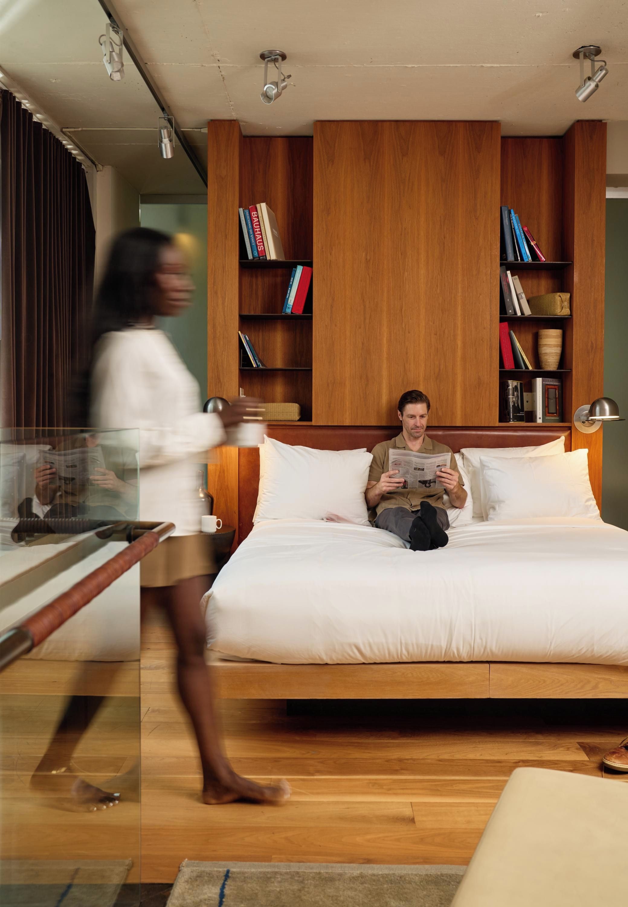 Une chambre moderne avec un grand lit, des étagères en bois et une cloison en verre.