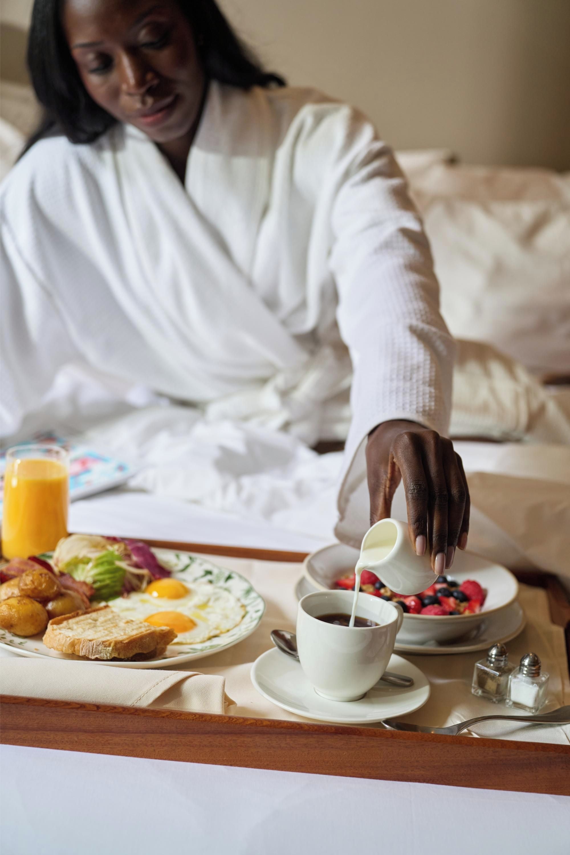 A person pouring milk into a cup of coffee on a tray with breakfast items.