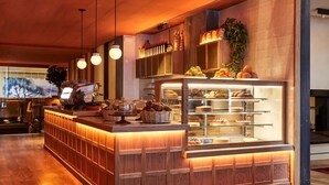 Mostrador de panadería con vitrina, mostrador de madera, luces colgantes y una planta.