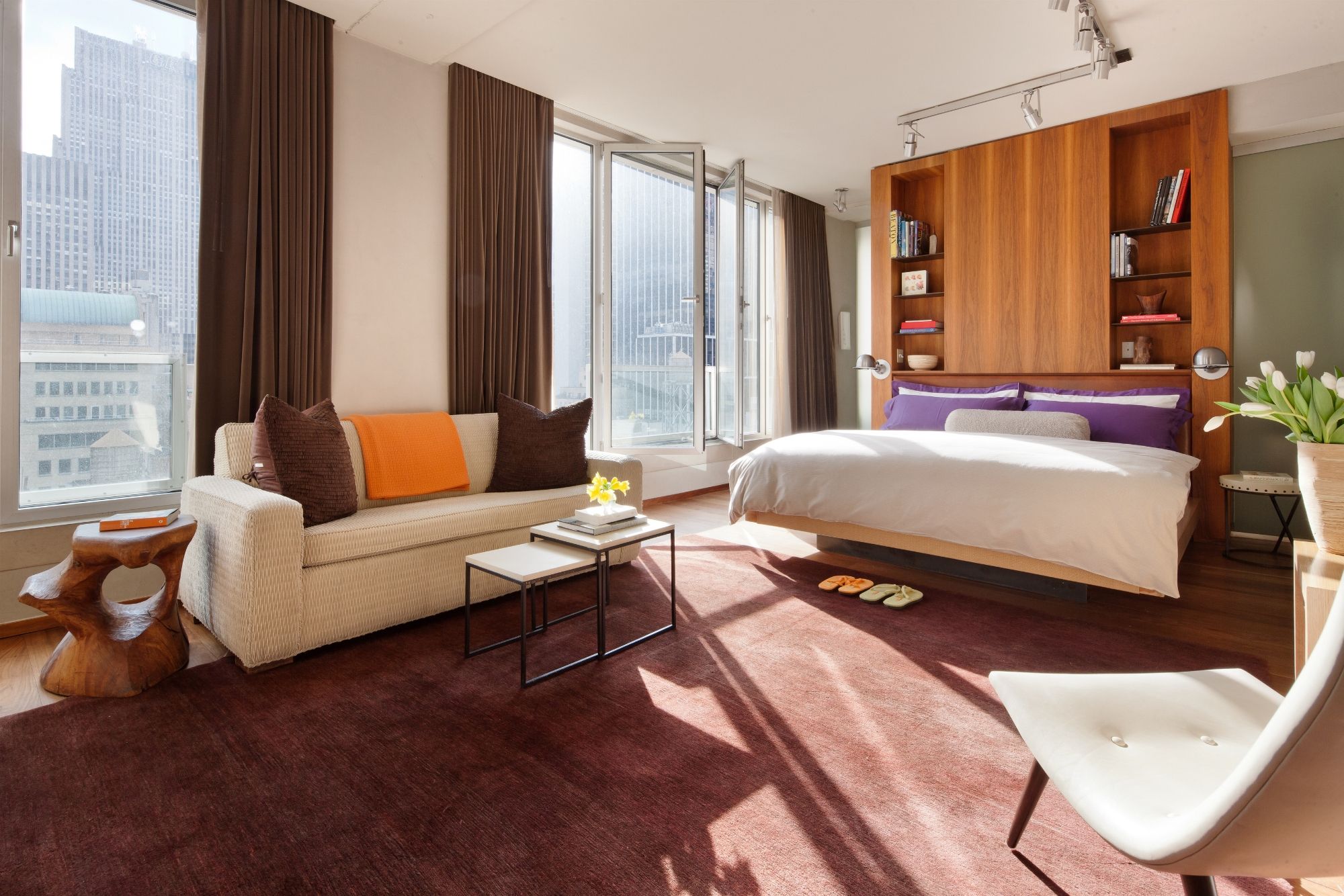 A modern hotel room with a large bed, a sofa, a coffee table, and a bookshelf.