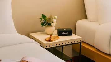 Una habitación de hotel moderna con una cama, una mesita de noche con una lámpara, una pequeña mesa con un jarrón de flores y una revista.