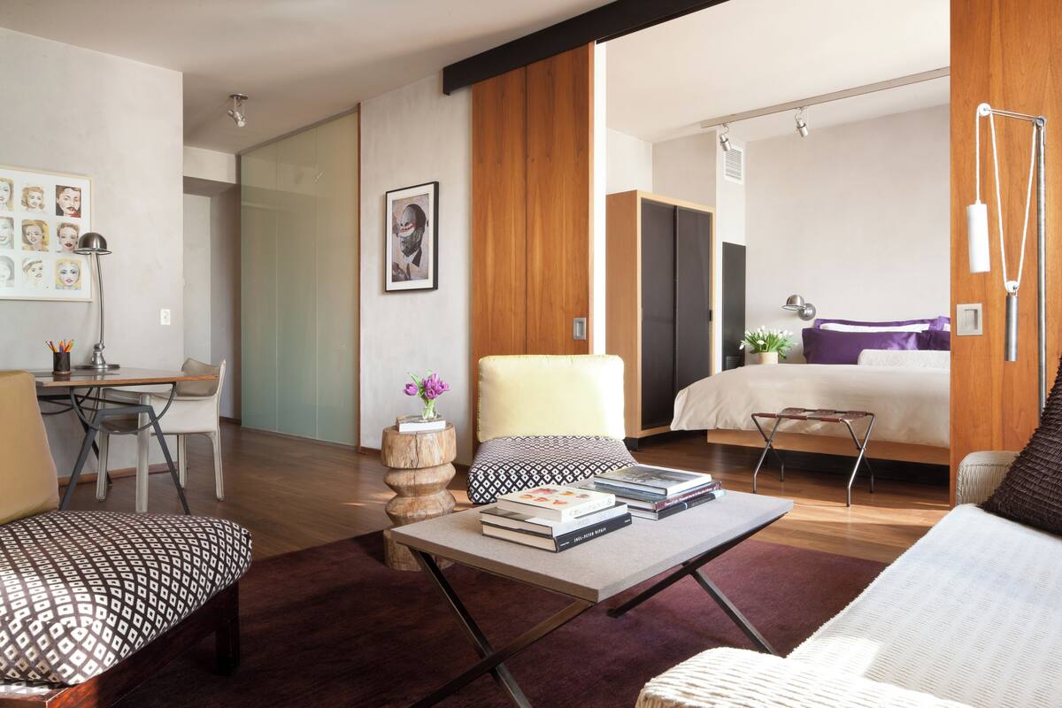Una habitación de hotel moderna con una cama, un sofá, una mesa de centro con libros, un escritorio y una silla.