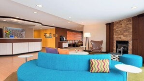A modern hotel lobby with a blue sofa, a fireplace, and a reception desk. - Fairfield Inn and Suites By Marriott St Charles (St. Charles)