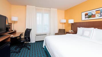 A hotel room with a bed, desk, chair, TV, and a window with curtains.