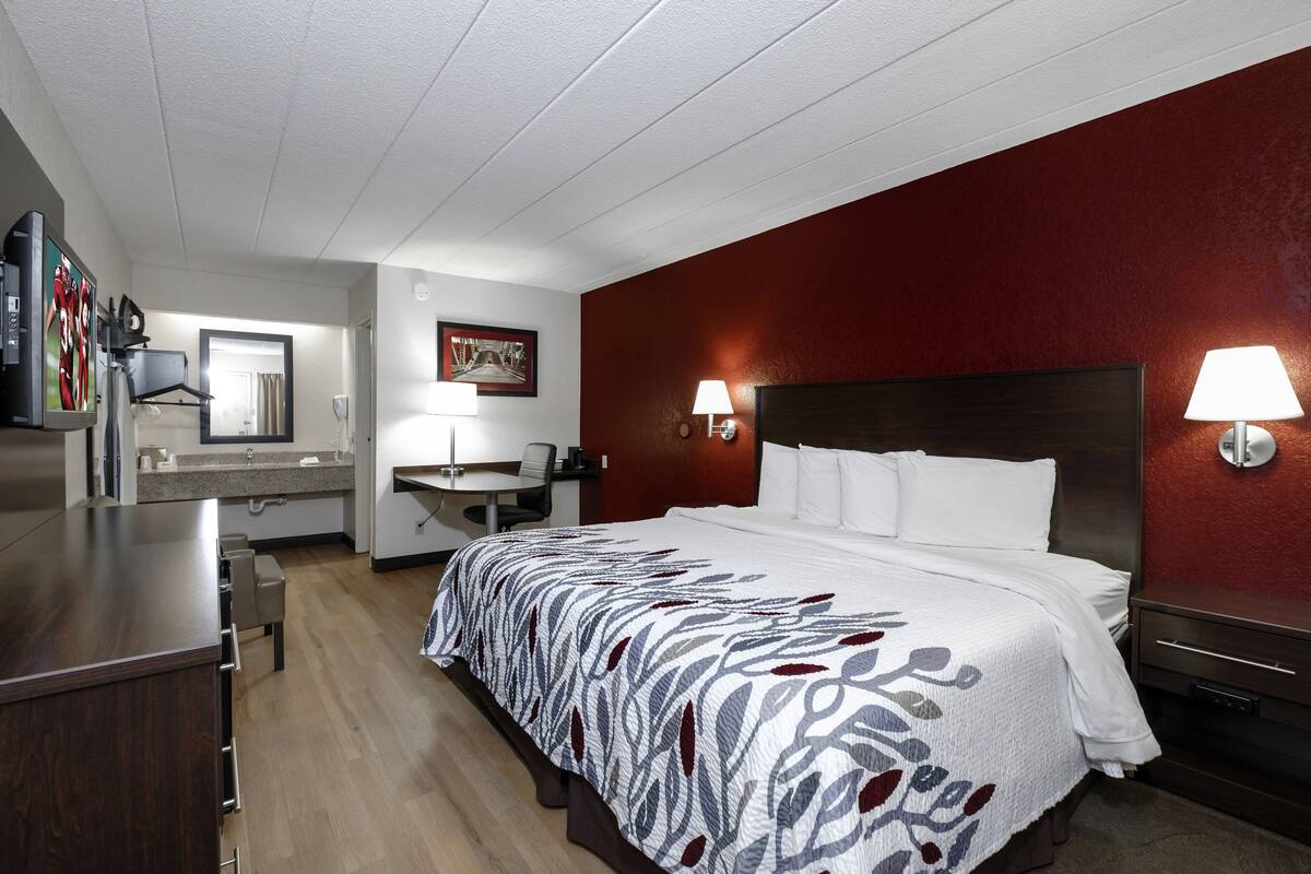 A hotel room with a bed, bedside lamps, a desk with a chair, a mirror, and a television.