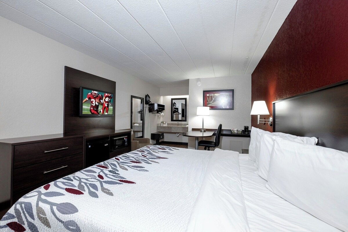 A hotel room with a bed, a desk, a chair, a television, and a bathroom mirror.