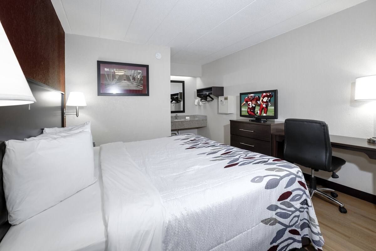 A hotel room with a bed, a desk, a chair, a television, and a bathroom.