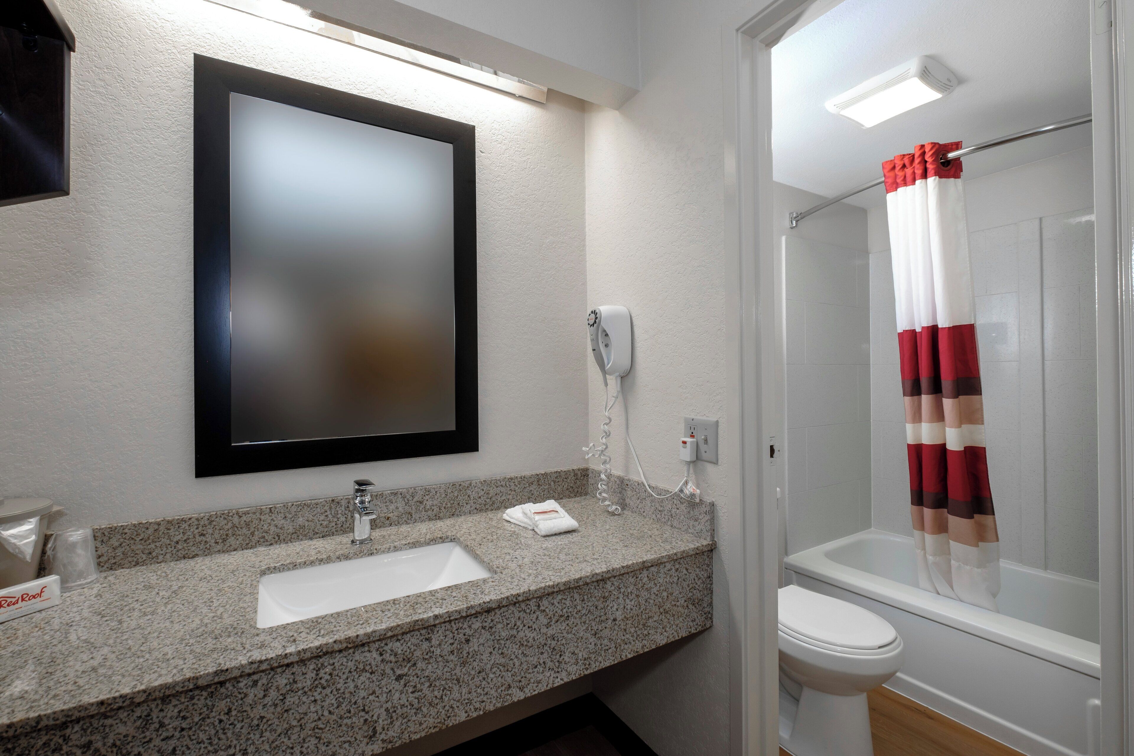 A bathroom with a granite countertop, a white sink, a mirror, a shower with a red and white striped curtain, and a toilet.