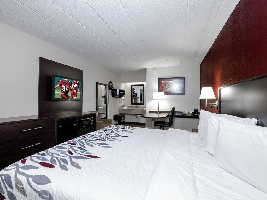 A hotel room with a bed, a desk, a television, and a bathroom mirror.