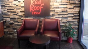 L’intérieur d’un Red Roof Inn, avec un mur en pierre, deux fauteuils en cuir, une petite table et une plante en pot.