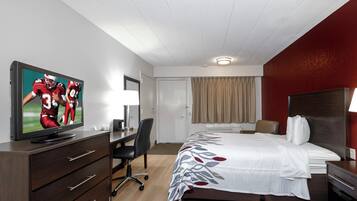Quarto de hotel com cama, escrivaninha, televisão e uma cadeira.