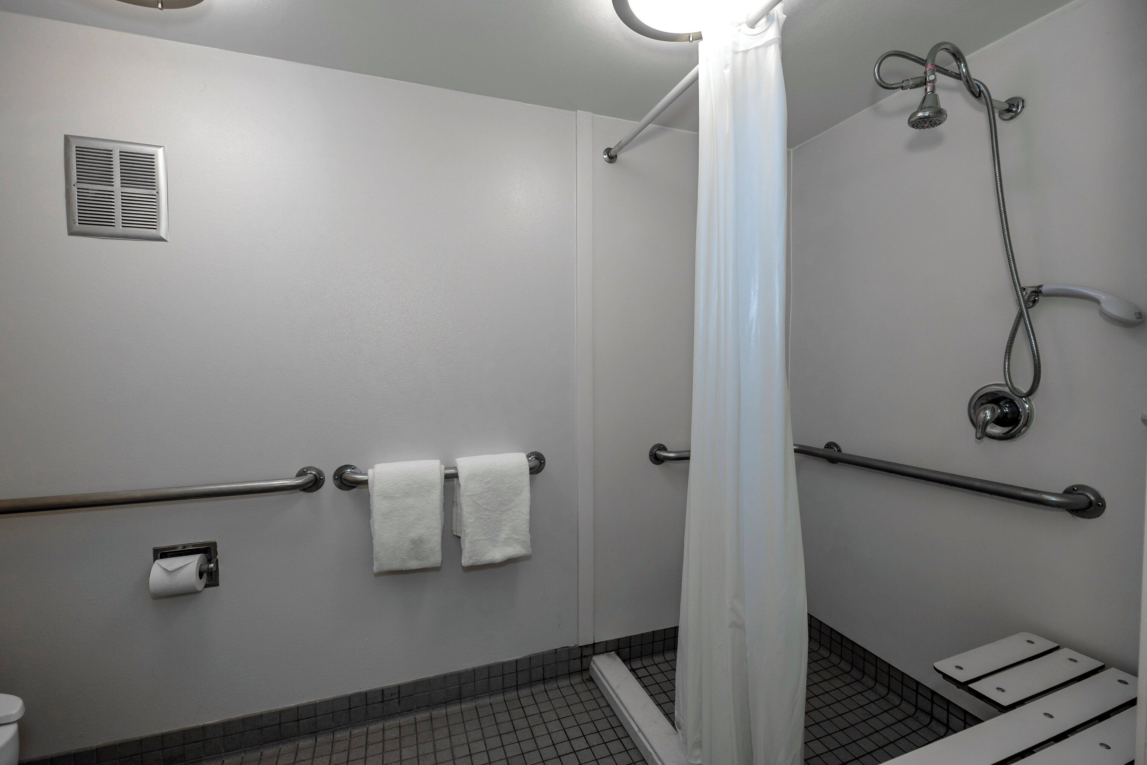 Un baño con ducha, barras de apoyo, inodoro y toallero.