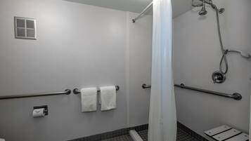 Un baño con ducha, barras de apoyo, inodoro y toallero.