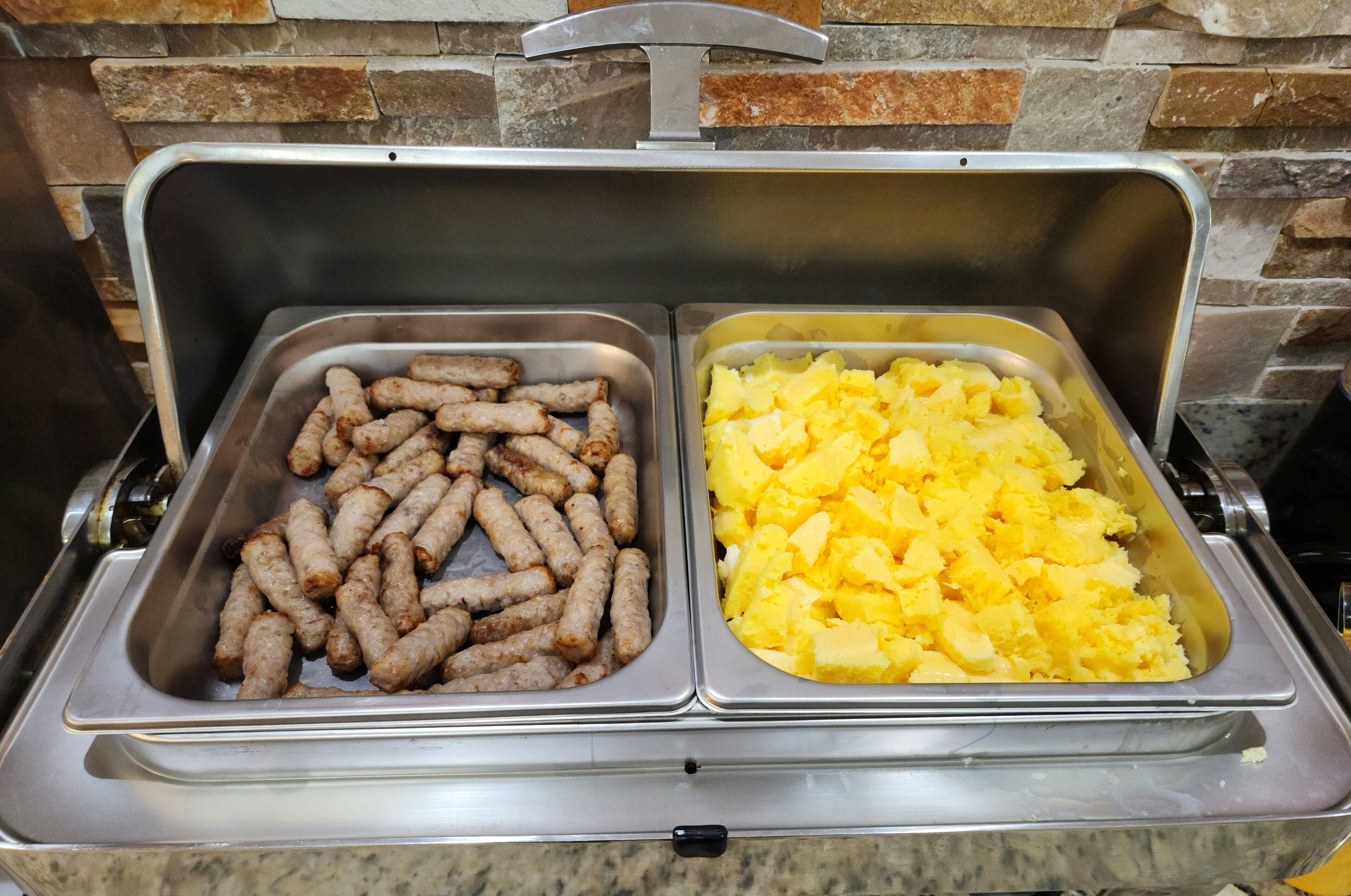 Un bufé con dos fuentes de comida: una con salchichas y otra con puré de papas.