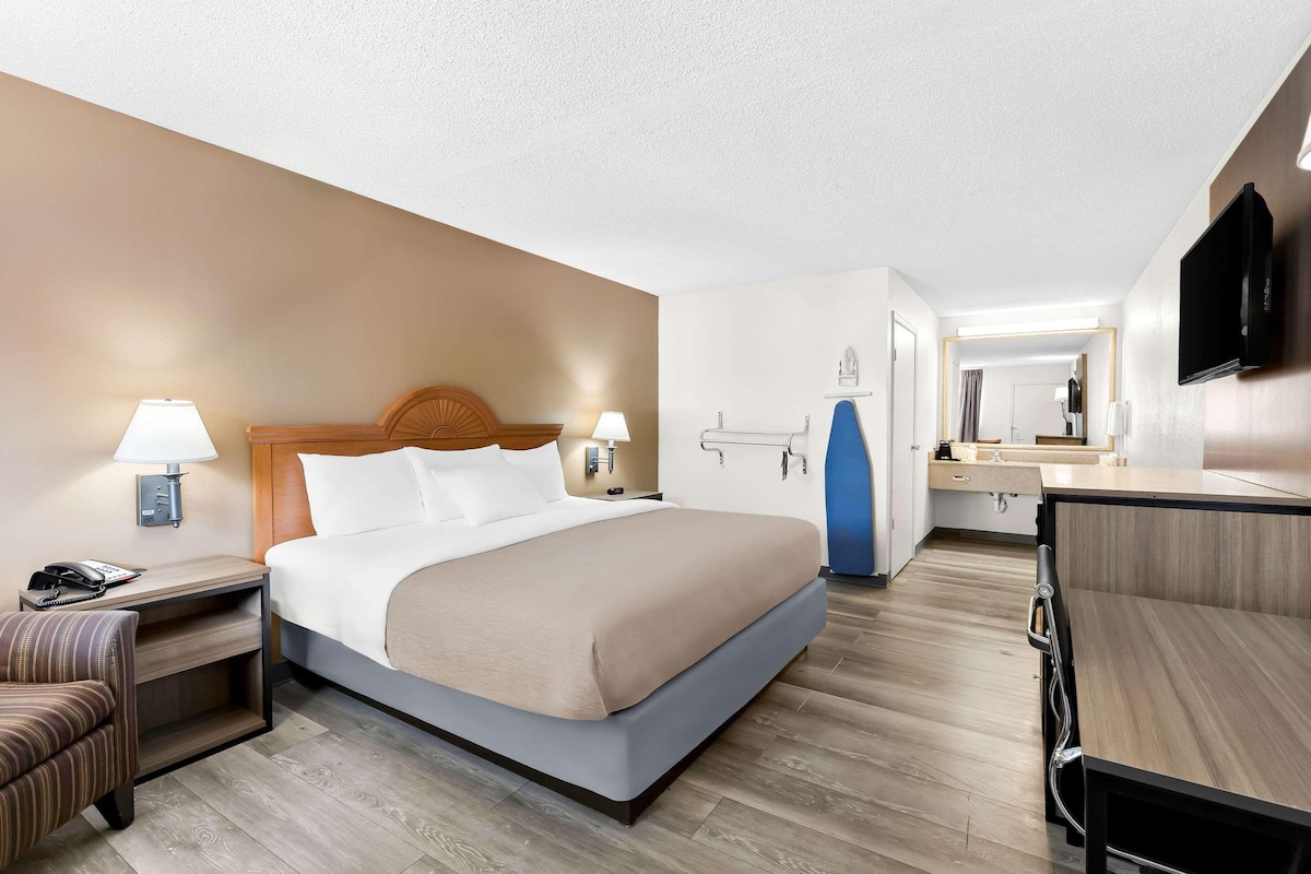A hotel room with a bed, bedside tables, a chair, a desk, a mirror, and a TV.