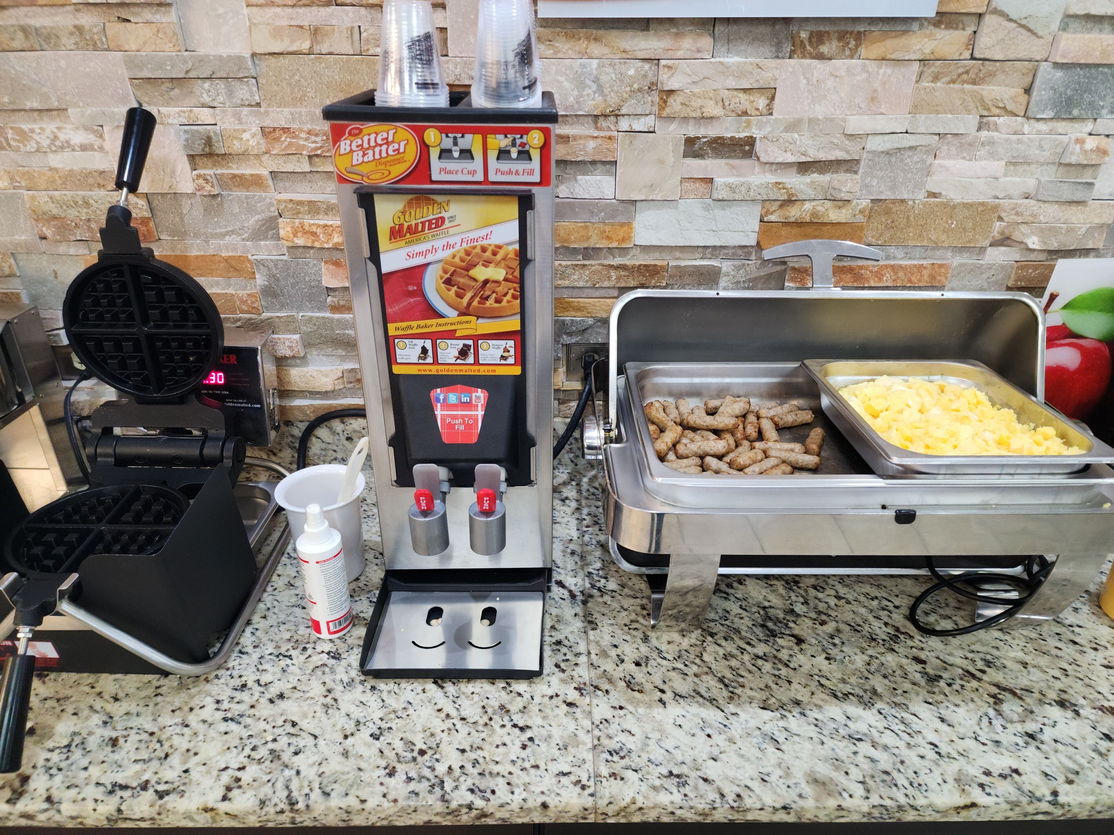 Uma máquina de waffles, um dispensador Better Batter e um buffet com salsichas e batatas.