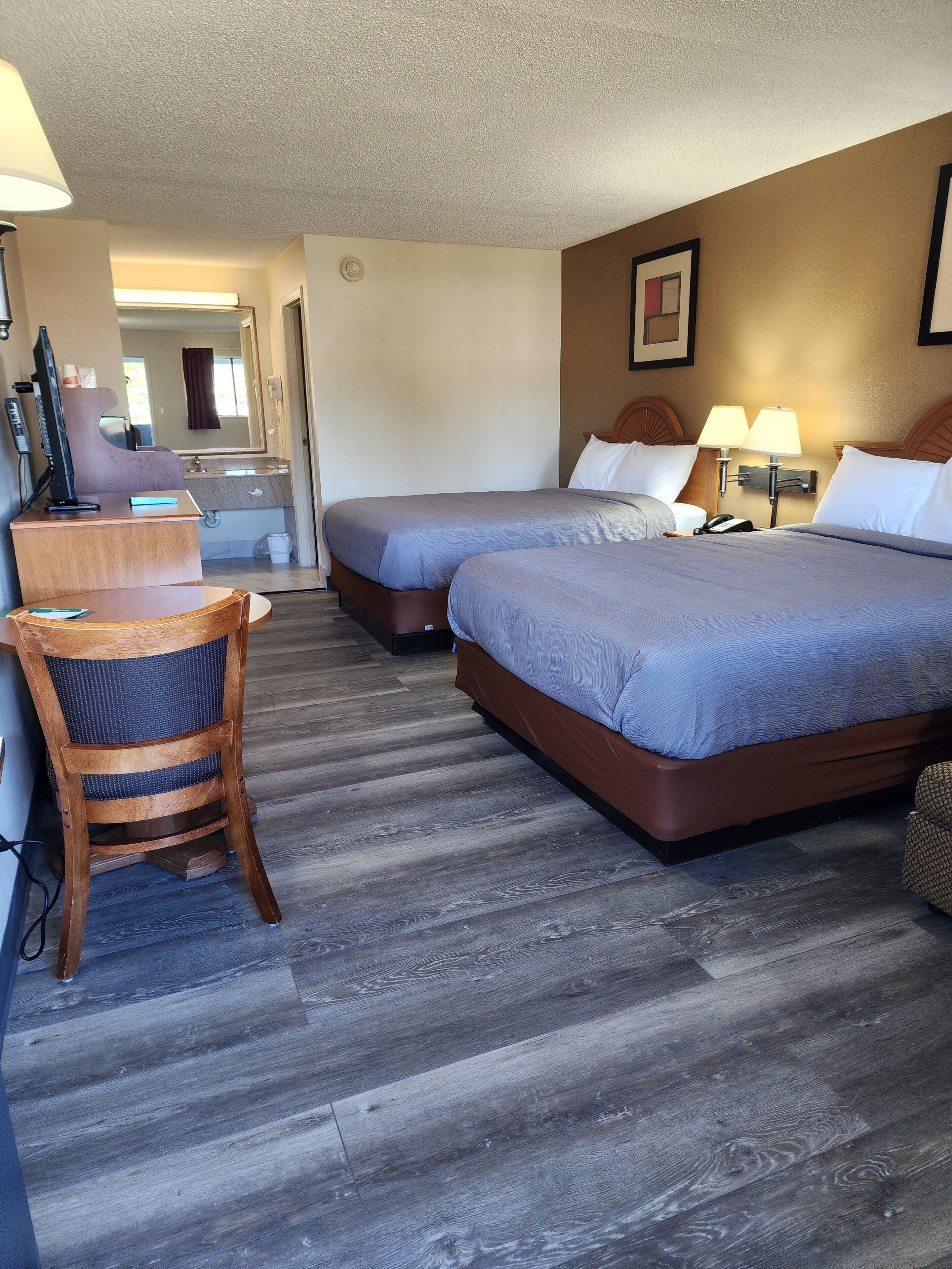 A hotel room with two beds, a desk, a chair, and a bathroom visible in the background.