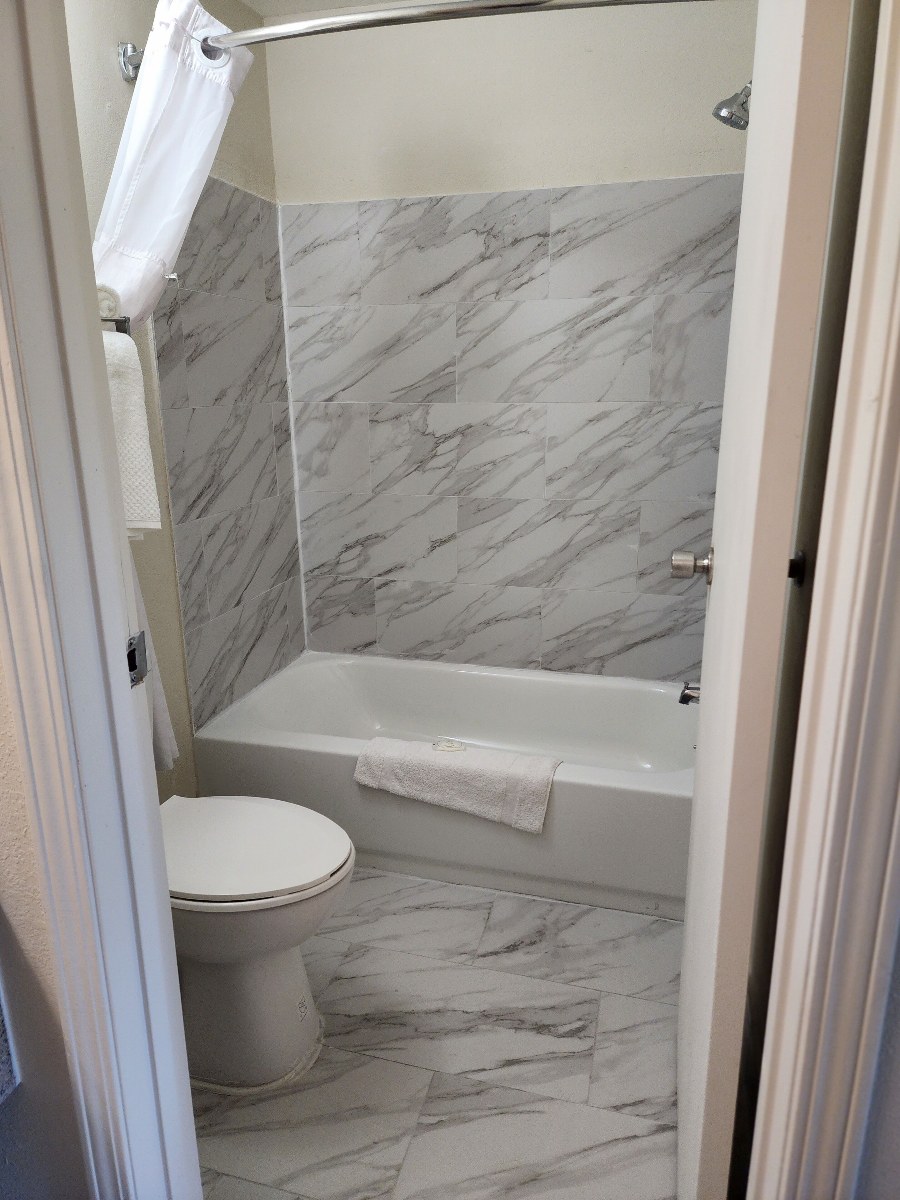 Un baño con inodoro, bañera y zona de ducha, todo revestido con diseños que imitan el mármol.