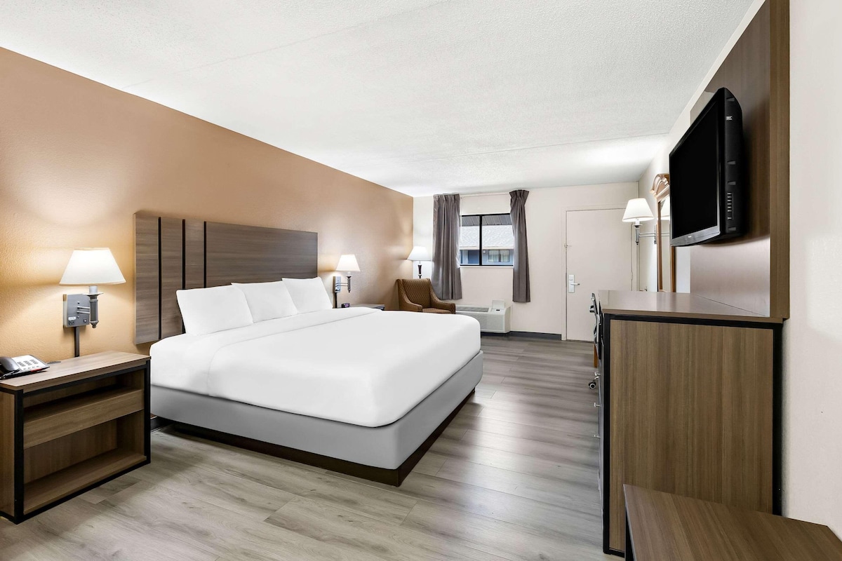 A hotel room with a large bed, bedside lamps, a flat-screen TV mounted on the wall, and a wooden nightstand.