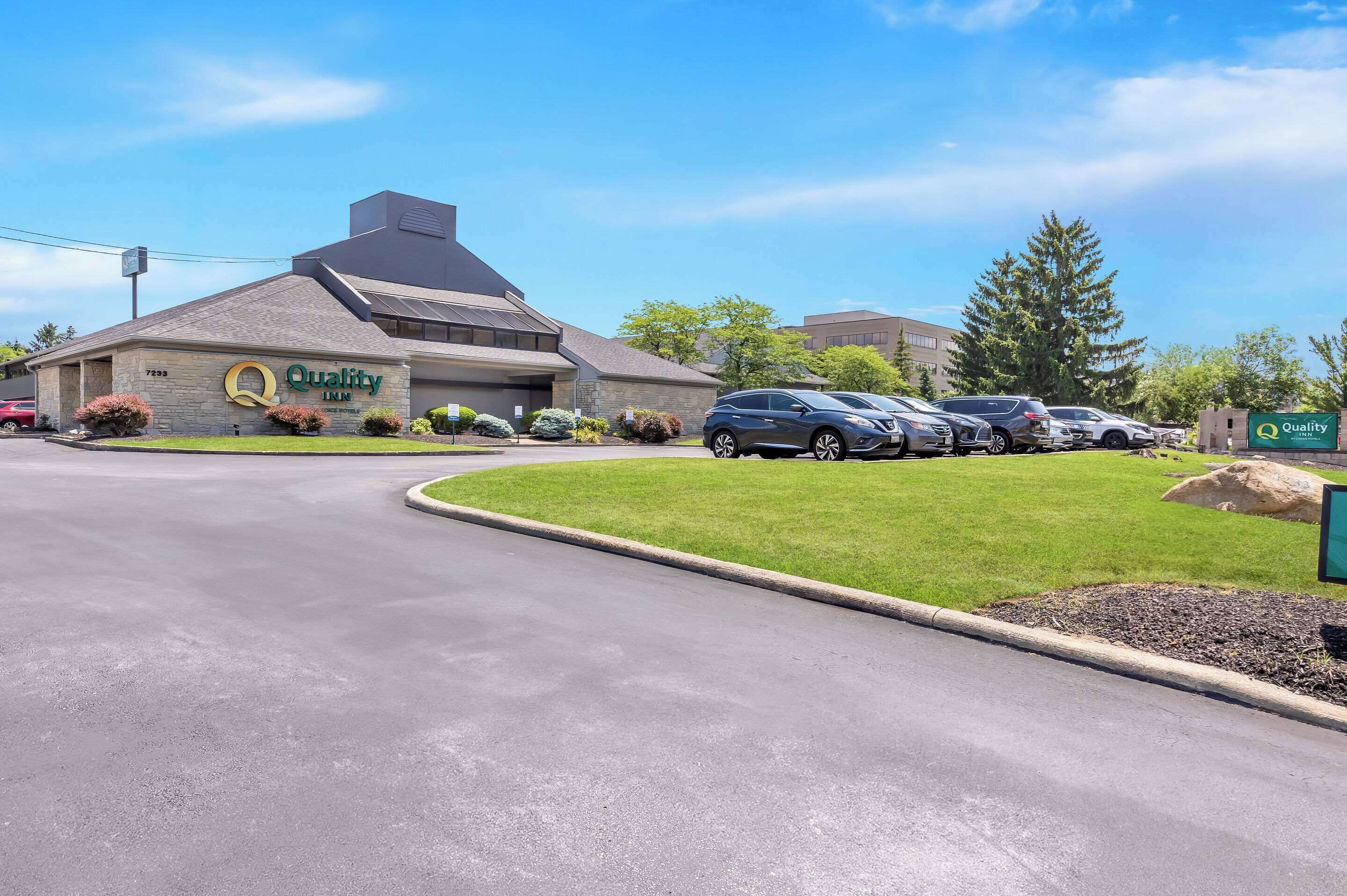 A Quality Inn hotel with a stone facade, a parking lot with several cars, and a well-maintained lawn.