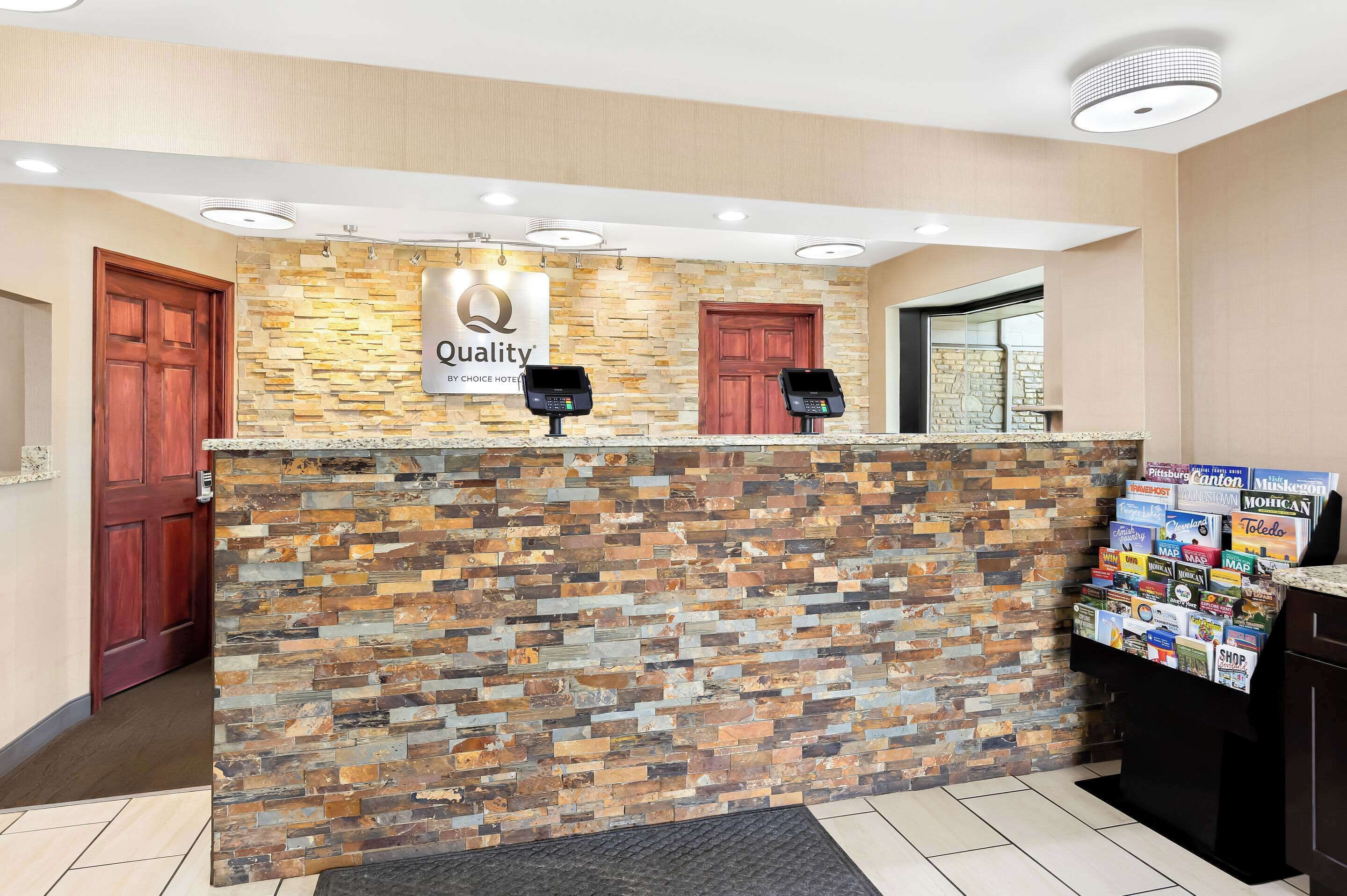 Zona de recepción con mostrador de textura pétrea, dos puertas de madera y un tablón de anuncios con folletos diversos.