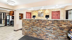 A hotel reception area with a stone wall, a 'Quality by Choice Hotels' sign, two wooden doors, and a reception desk with a computer and phone. - Quality Inn Middleburg Heights near Cleveland Airport (Middleburg Heights)