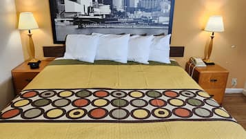 A hotel room with a bed, two bedside lamps, a framed cityscape picture, and a patterned bedspread.