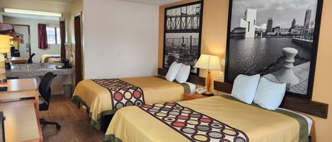 A hotel room with two beds, a desk, a chair, a lamp, and a large cityscape painting on the wall.