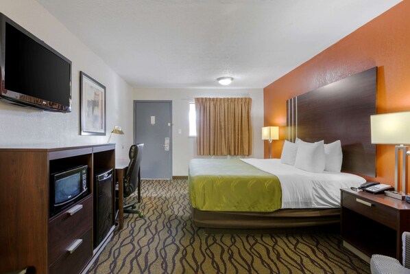 A hotel room with a bed, a desk with a lamp, a television, and a microwave. - Quality Inn Columbus - East (Columbus)