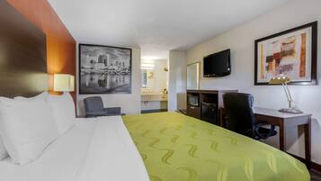 Una habitación de hotel con cama, escritorio, silla, televisión y obras de arte en las paredes.