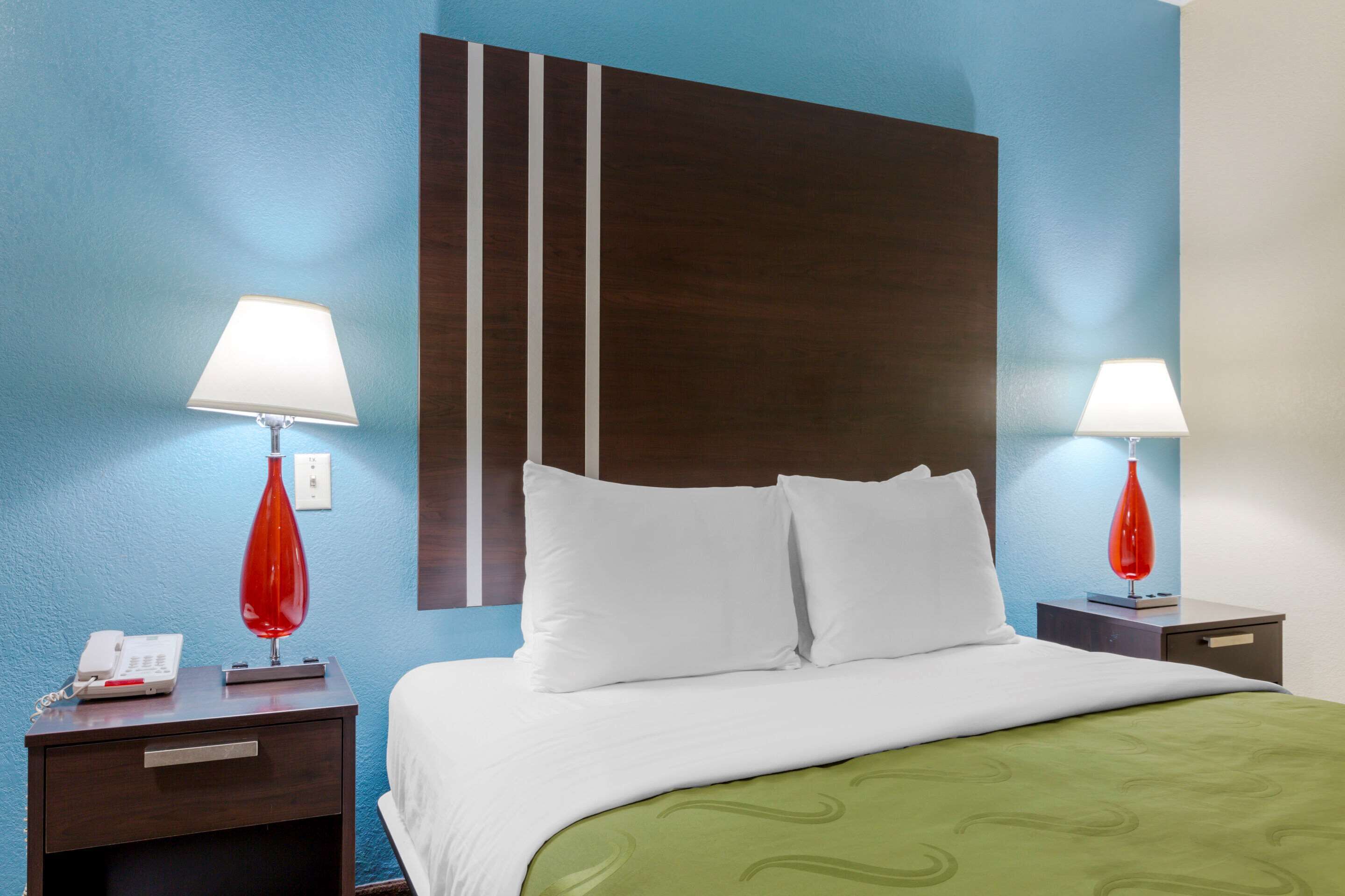 A hotel room with a bed, two nightstands, a telephone, and two red lamps.