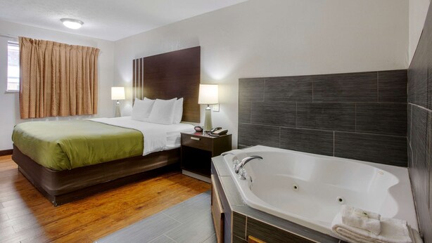 A hotel room with a bed, bedside table, lamp, and a large bathtub. - Quality Inn Columbus - East (Columbus)