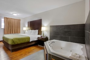 A hotel room with a bed, bedside table, lamp, and a large bathtub. - Quality Inn Columbus - East (Columbus)