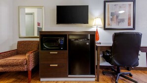 A compact hotel room with a kitchenette, a flat-screen TV, a framed artwork, and a patterned armchair. - Quality Inn Columbus - East (Columbus)