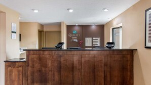 A reception desk with a wooden finish, a "Quality Inn" sign, a phone, and a self-service kiosk. - Quality Inn Columbus - East (Columbus)