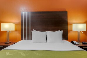 A hotel room with a large bed, two bedside lamps, a telephone, and a wooden headboard.