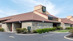 A Quality Inn with a stone facade, a red roof, and a parking lot in front. - Quality Inn Columbus - East (Columbus)