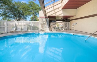 Una piscina azul cristalina con un muelle de madera y sillas de metal blanco.