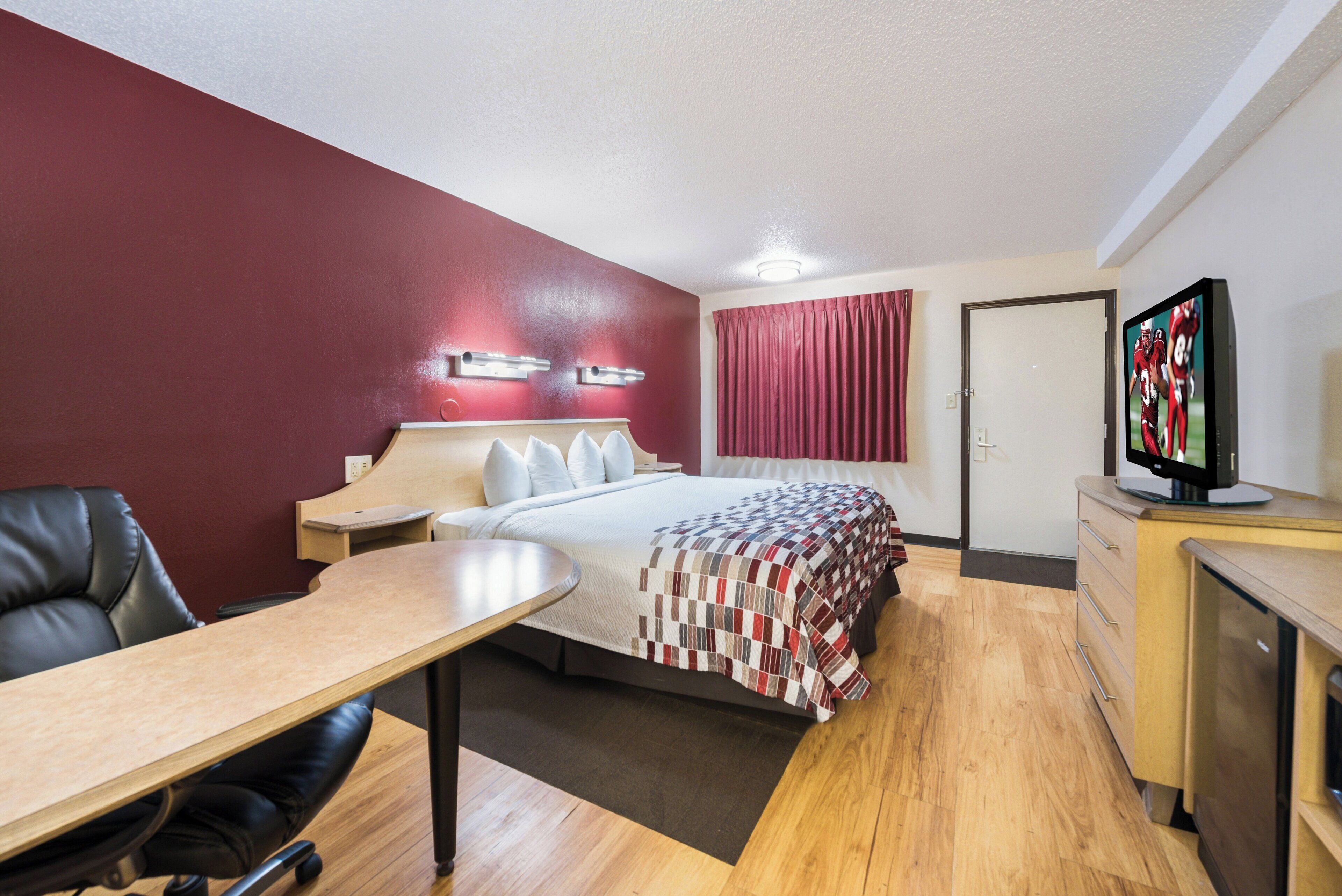 Una habitación de hotel con cama, escritorio, silla, televisor y puerta.