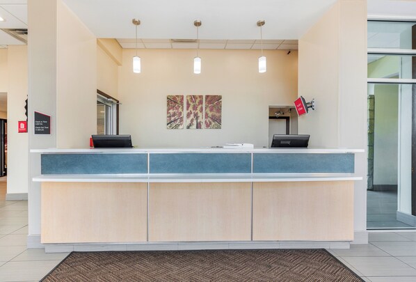 A reception desk with a check-in/out sign, a digital display, and a wall-mounted sign indicating free Wi-Fi.