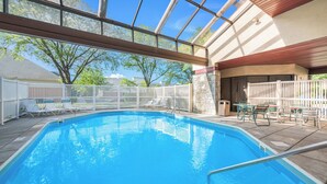 An indoor swimming pool with clear blue water, surrounded by a white fence, and a patio area with chairs and tables. - Red Roof Inn Columbus - Grove City (Grove City)
