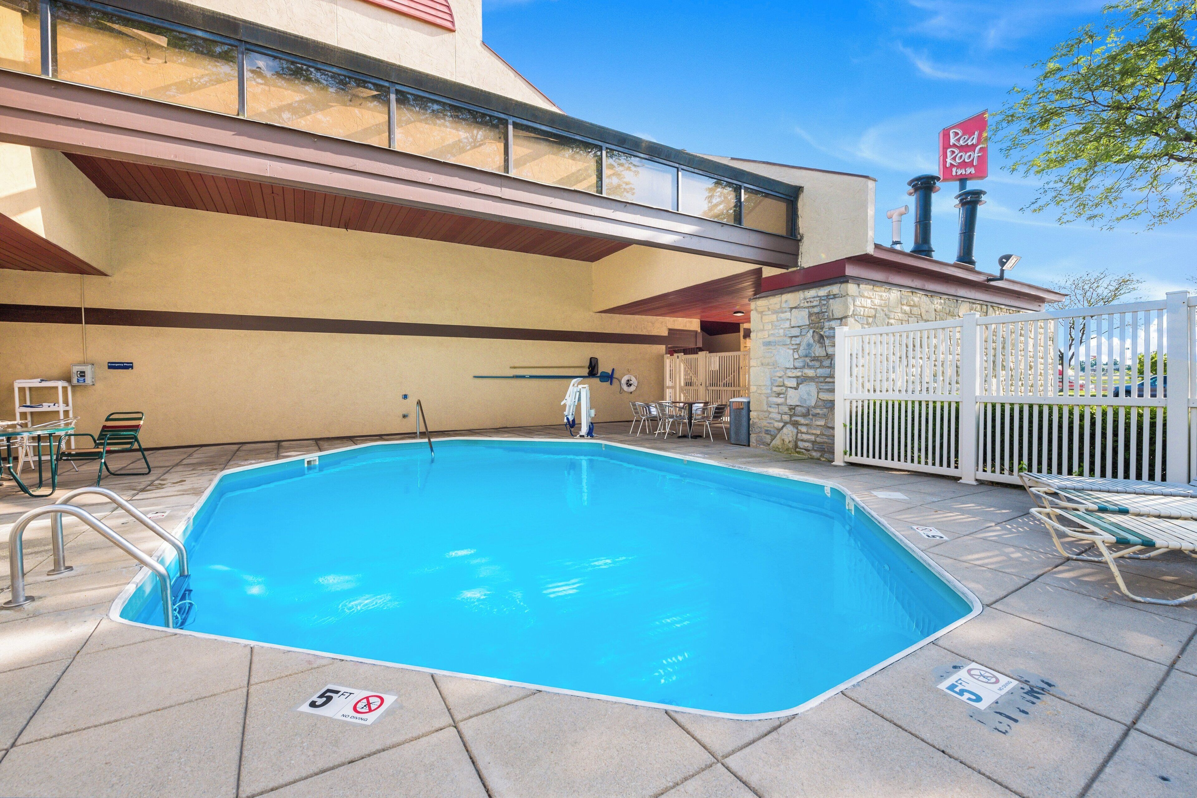 Une piscine extérieure avec un poste de surveillance pour le sauveteur, un panneau indiquant qu’il est interdit de plonger et une enseigne Red Roof Inn.