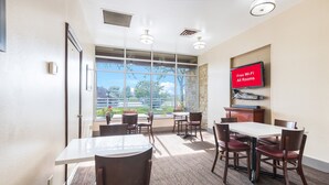 A conference room with a large table and chairs, a television screen displaying "Free Wi-Fi All Rooms," and a view of a green landscape through large windows.